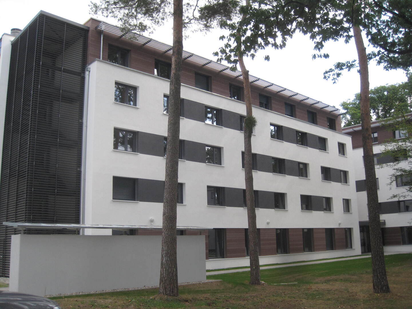 Moderne Wohnanlage mit weißen und grauen Fassaden, umgeben von Bäumen und Grünflächen.